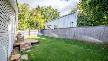 A backyard with a wooden deck, a barbecue grill, and a stone pathway.
