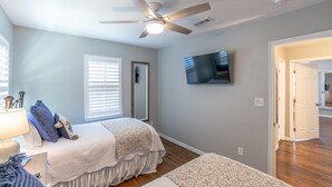 A bedroom with a bed, a ceiling fan, a TV, and a door leading to another room. - Cozy cottage, just a short walk to UofA (Fayetteville)