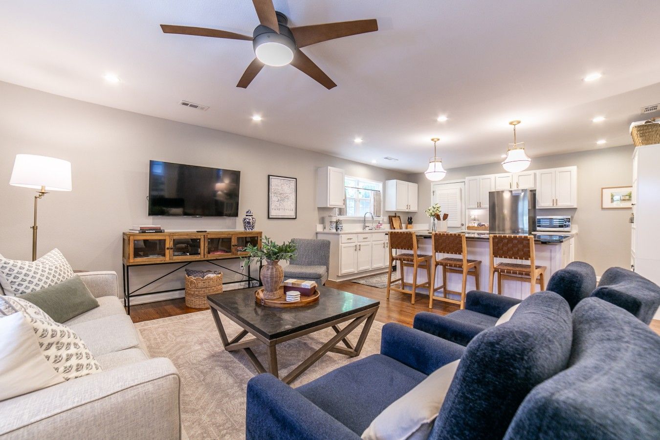 Una sala moderna con sofá, mesa de centro y televisor. Hay una cocina con mesa y sillas.