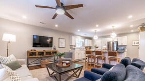 A modern living room with a sofa, a coffee table, and a TV. There is a kitchen area with a dining table and chairs. - Cozy cottage, just a short walk to UofA (Fayetteville)