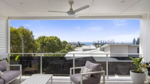 A balcony with a white ceiling fan, a glass balustrade, and a view of the sea and trees. - Sun Crest - amazing ocean views, walk to beach and vibrant village of Woolgoogla (Woolgoolga)