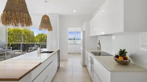 A modern kitchen with white cabinetry, a central island, and a view to the outdoors. - Sun Crest - amazing ocean views, walk to beach and vibrant village of Woolgoogla (Woolgoolga)