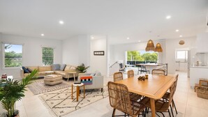 A spacious living area with a dining table, sofas, and a kitchen in the background. - Sun Crest - amazing ocean views, walk to beach and vibrant village of Woolgoogla (Woolgoolga)