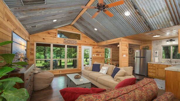 A cozy cabin interior with wooden walls, a ceiling fan, a kitchenette, and large windows offering a view of the outdoors. - Riverside Cabin | Kayaks | Mountains | Stargazing (Nashoba)