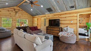 A cozy cabin interior with a wooden interior, a ceiling fan, a flat-screen TV, and a fireplace. - Riverside Cabin | Kayaks | Mountains | Stargazing (Nashoba)