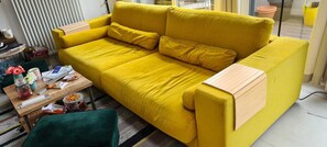 A bright yellow sofa with cushions, a wooden side table, a green chair, and a small table with various items. - Loft Apartment - City Center (Cluj Napoca) (Cluj-Napoca)
