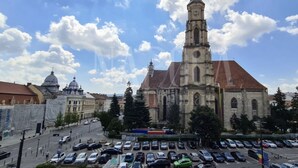 Una chiesa con un campanile alto e una torre dell'orologio, circondata da auto parcheggiate e alberi.