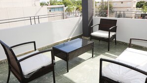 Een balkon met rieten meubilair, een tafel met glazen blad en uitzicht op de skyline.