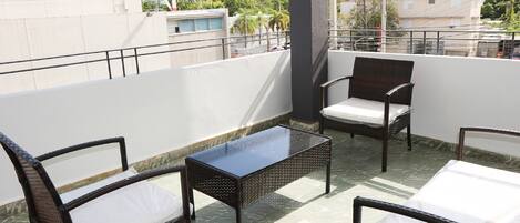 A balcony with wicker furniture, a glass-top table, and a view of the cityscape.