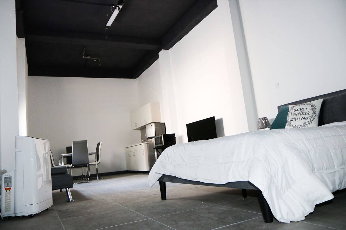 A bedroom with a bed, a desk, a chair, a refrigerator, and a microwave.
