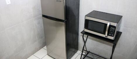 A compact kitchen with a stainless steel refrigerator and a microwave on a small black metal stand.