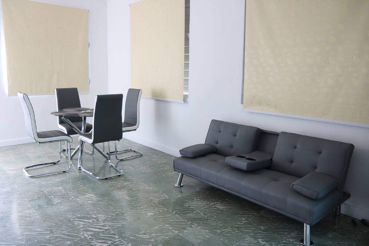 A modern room with a glass table, black chairs, a grey sofa, and beige curtains.