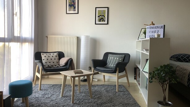 A modern living room with a sofa, armchair, small table, and a bookshelf.