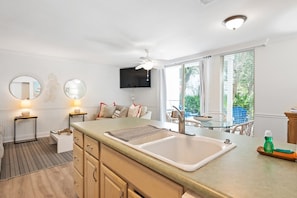 A modern kitchen with a large sink, a dining area with a glass table, and a TV mounted above the counter.