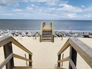 A wooden staircase leading to a beach with a rocky shoreline and the ocean in the background.