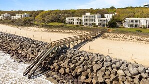 Ein Strandresort mit einer Holzpromenade, die zu einer felsigen Küste führt, umgeben von modernen Gebäuden mit Balkonen.