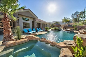 A swimming pool with lounge chairs, a palm tree, and a building with large windows.