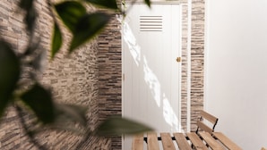 A wooden table and bench in a corner with a stone wall and a white door.
