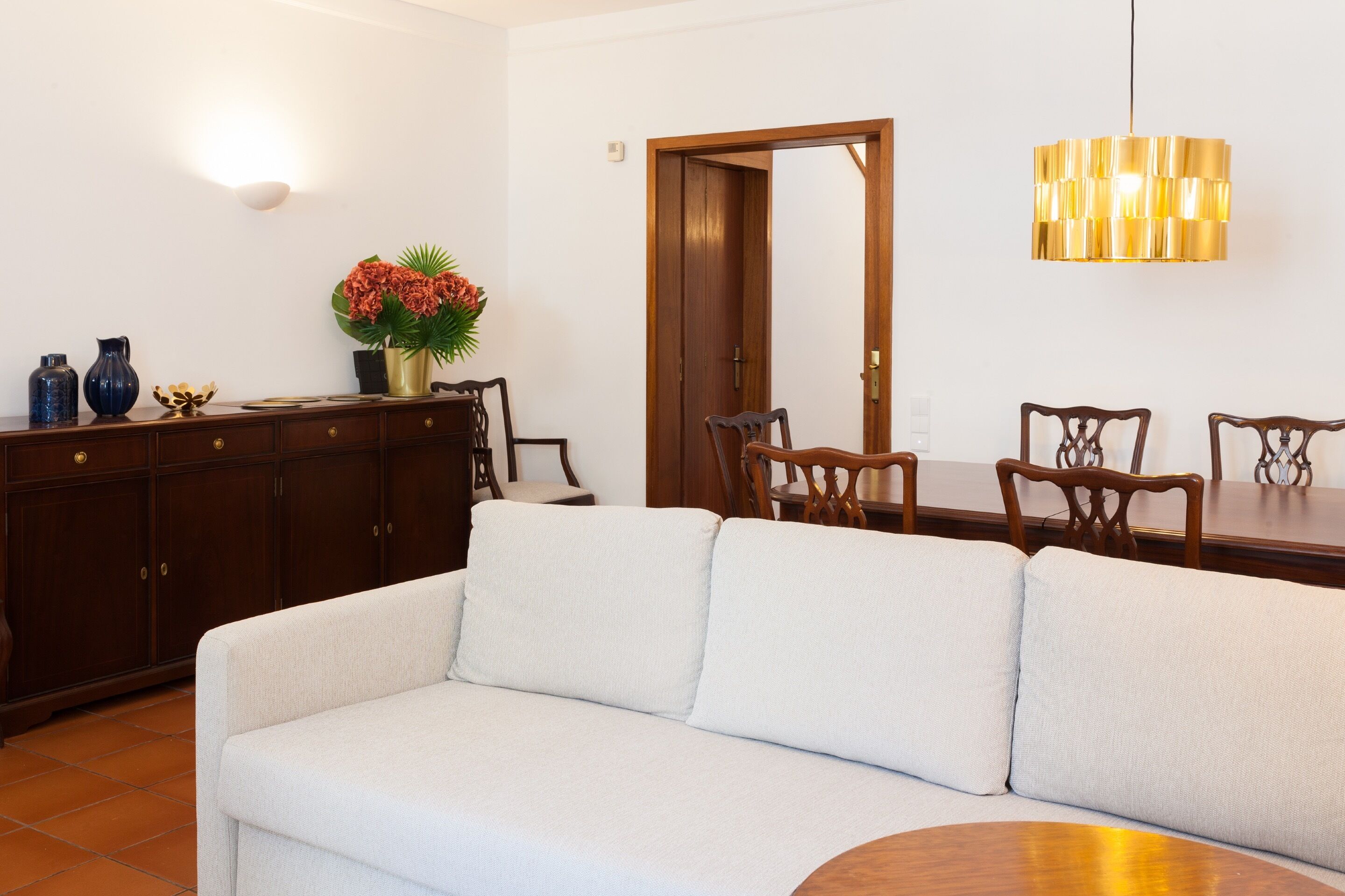 Ein Wohnzimmer mit einer Couch, einem Holzesstisch mit Stühlen, einem Schrank und einer Wandleuchte.