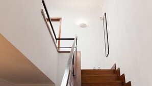 A staircase with wooden steps and a metal handrail, leading to a landing with a light fixture and a framed picture on the wall.