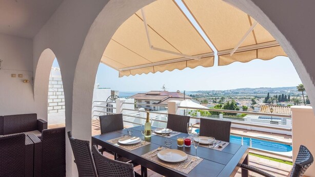 Una terraza con mesa lista para comer, con vista a una piscina y al paisaje urbano.