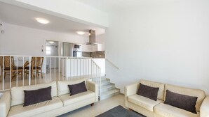 Una sala moderna con dos sofás color crema, una escalera y una zona de cocina con microondas y horno.