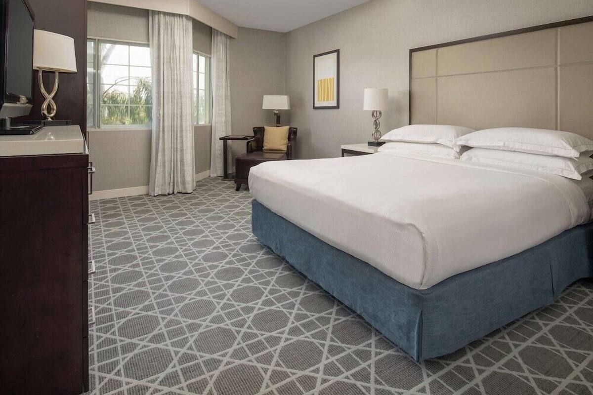 A hotel room with a large bed, a desk, a chair, and a window with curtains.