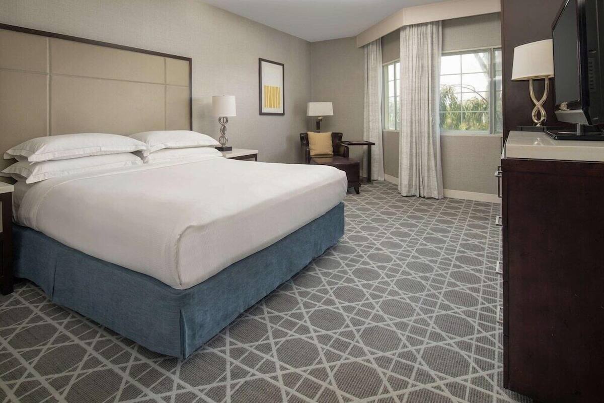 A hotel room with a large bed, a desk, a chair, and a TV.