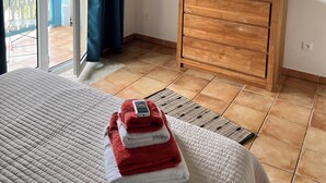 A bedroom with a bed, a wooden dresser, a painting of Baie Orientale, and a view through the open door. - Maison 90 m2 Pour 4 Personnes Avec Piscine Collective (Orient baie)