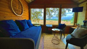 A cozy cabin interior with a wooden ceiling, a blue sofa, a small table, and a chair. - THE JACK: A Beautiful Treehouse Suite overlooking the Texas Hill Country (Dripping Springs)