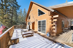 Enjoy outdoor seating on the deck with a bench and table, surrounded by a wooded area.