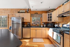 Compact kitchen with a stainless steel refrigerator, black countertop, and a window with a plaid curtain.