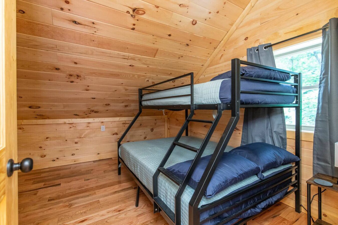 Dormitorio con literas, paredes de madera y ventana con cortinas.