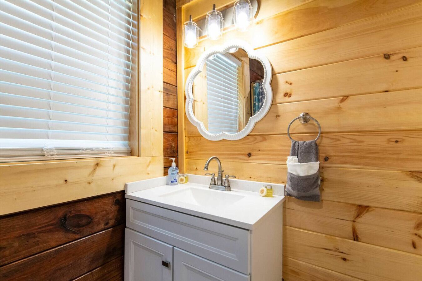 Une salle de bain rustique, avec des murs en bois, un lavabo blanc, un miroir et un porte-serviettes.