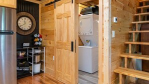 Una cocina funcional con armarios de madera, un refrigerador de acero inoxidable, una lavadora y un reloj en la pared.