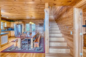 A wooden cabin interior with a kitchen, dining area, and a staircase. - In The Heights - Hot Tub | Fire Pit | Game Room | Mountain Views (Morganton)
