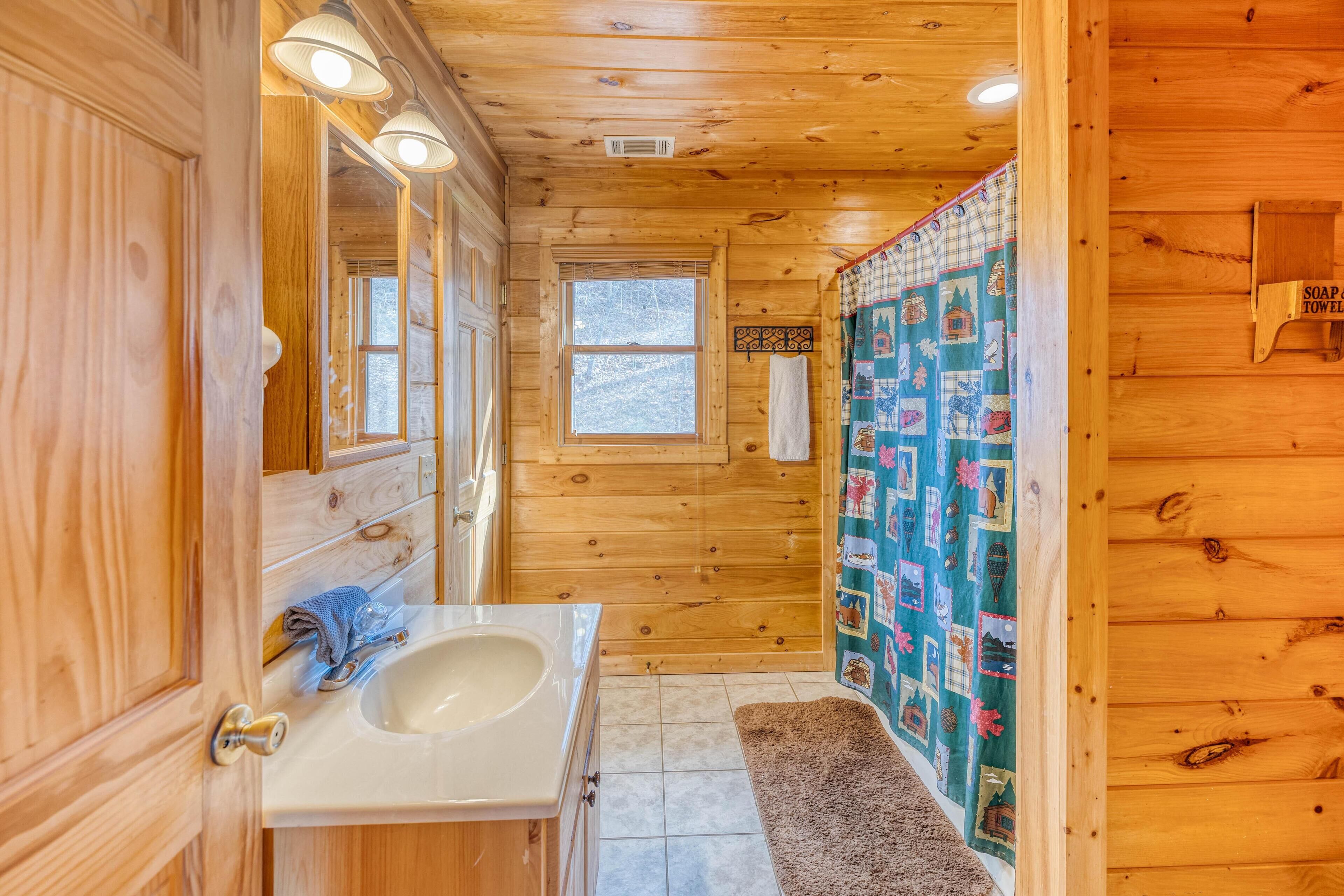 A wooden cabin bathroom with a sink, mirror, and a window.