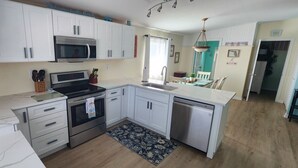 A modern kitchen with white cabinets, a built-in oven, microwave, and dishwasher. There is a small island with a sink and a window above the sink. - Lower Keys paradise (Cudjoe Key)