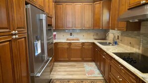 A kitchen with wooden cabinets, a stainless steel refrigerator, a tiled backsplash, and a patterned rug. - Haggville Hacienda - Private Riverfront @Vacation Frio River - Pool Sleeps 29-38 (Concan)
