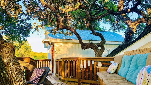 Eine Holzterrasse mit einer Sitzecke, einem Baum und einem Gebäude mit Metallbedachung.