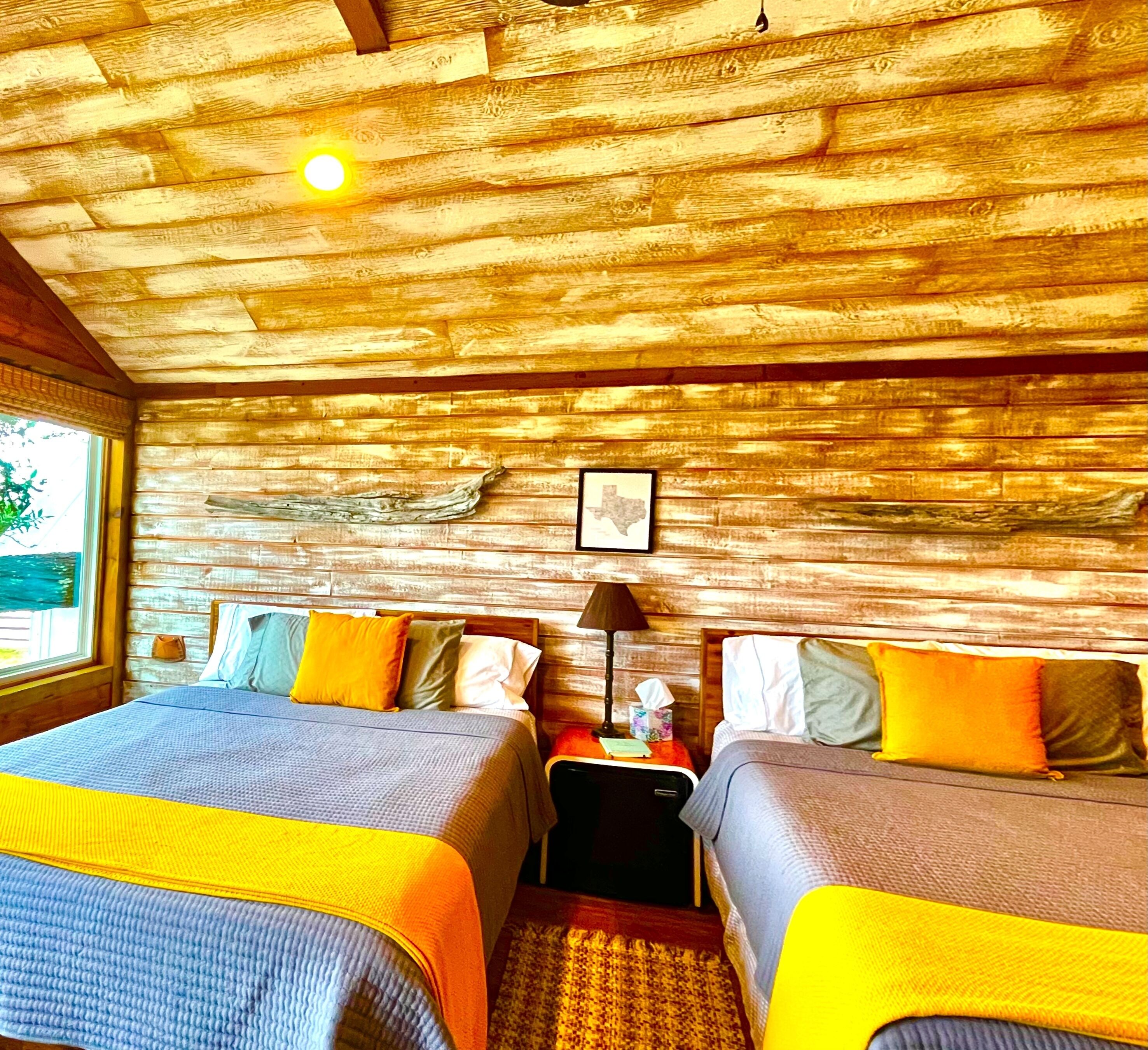 Une chambre avec deux lits, des murs en bois, une fenêtre et une carte encadrée accrochée au mur.
