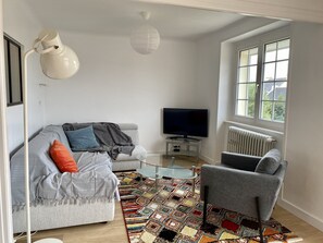A modern living room with a sofa, armchair, TV, and a patterned rug.
