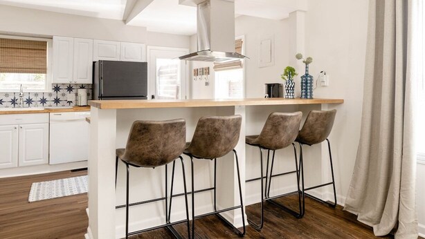 Een moderne keuken met witte kasten, een zwarte koelkast, een rvs afzuigkap en een houten aanrecht.