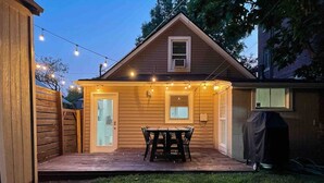 Een houten huis met een overdekte patio, een tafel, stoelen en lichtjes.