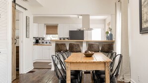 Een eetgedeelte met een houten tafel en zwarte stoelen, een keuken op de achtergrond, en een witte inrichting.