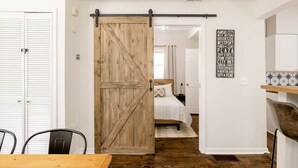 Een kamer met een houten schuifdeur naar een slaapkamer met een bed en een witte muur met een stadsbord.