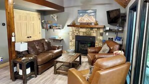 A living room with a stone fireplace, leather sofas, a coffee table, and a television. - Rustic, Cozy Cabin with a View of the Smokies, Firepit, Large Deck, Pet-Friendly (Almond)