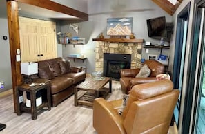A living room with a stone fireplace, leather sofas, a coffee table, and a television. - Rustic, Cozy Cabin with a View of the Smokies, Firepit, Large Deck, Pet-Friendly (Almond)