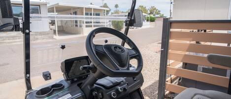 A golf cart interior with a steering wheel, control panel, and seating area.