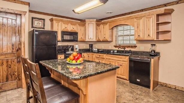 Una cocina con armarios de madera, encimera de granito, refrigerador negro, microondas, cafetera y licuadora.